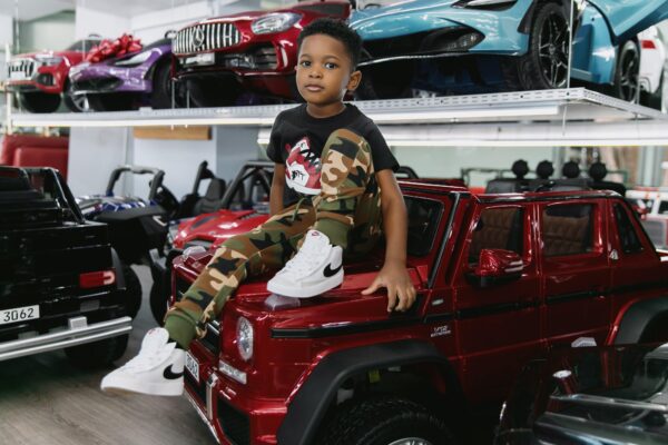 Boy sitting on a Mercedes G-Wagon Wearing Air Bear T-Shirt in Black With Camouflage Sweatpants and Nike Running Shoes